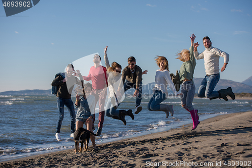 Image of young friends jumping together at autumn beach