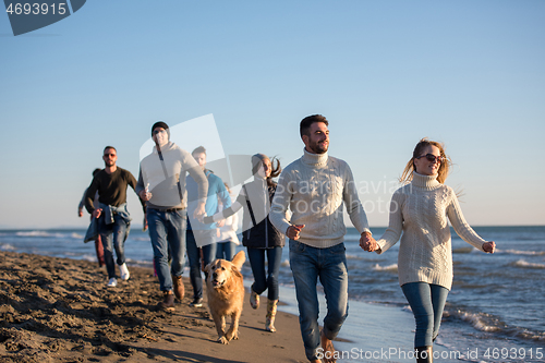 Image of Group of friends running on beach during autumn day