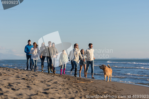 Image of Group of friends running on beach during autumn day