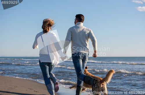 Image of couple with dog having fun on beach on autmun day