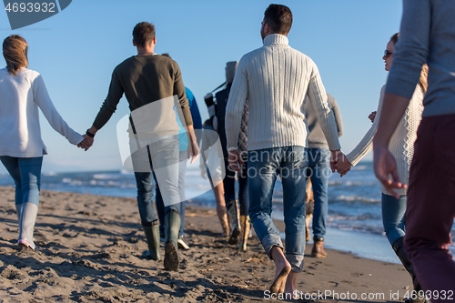 Image of Group of friends running on beach during autumn day