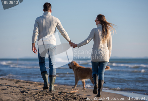 Image of couple with dog having fun on beach on autmun day