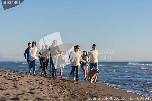 Image of Group of friends running on beach during autumn day