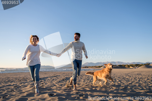 Image of couple with dog having fun on beach on autmun day