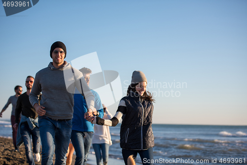 Image of Group of friends running on beach during autumn day