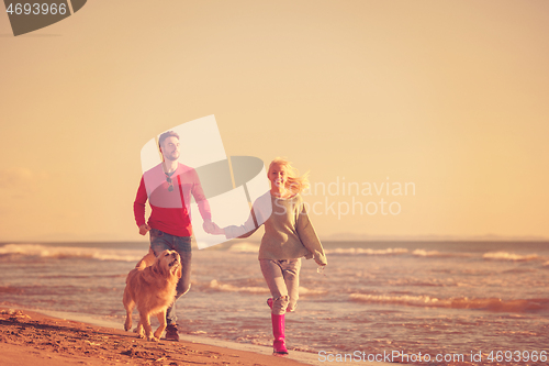 Image of couple with dog having fun on beach on autmun day