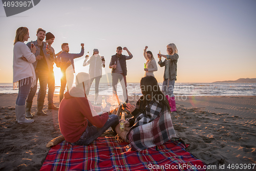 Image of Couple enjoying with friends at sunset on the beach