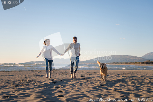 Image of couple with dog having fun on beach on autmun day