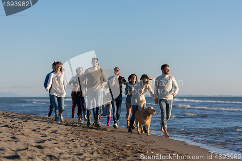 Image of Group of friends running on beach during autumn day