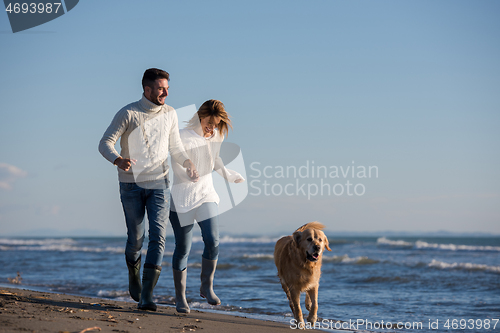 Image of couple with dog having fun on beach on autmun day