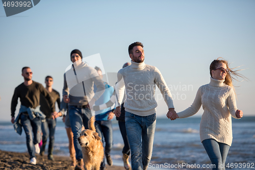 Image of Group of friends running on beach during autumn day