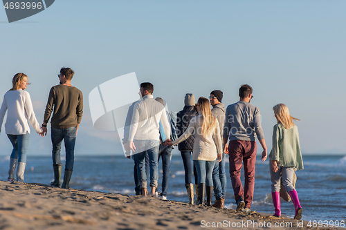 Image of Group of friends running on beach during autumn day