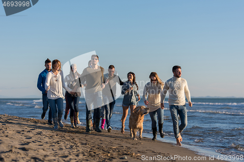 Image of Group of friends running on beach during autumn day