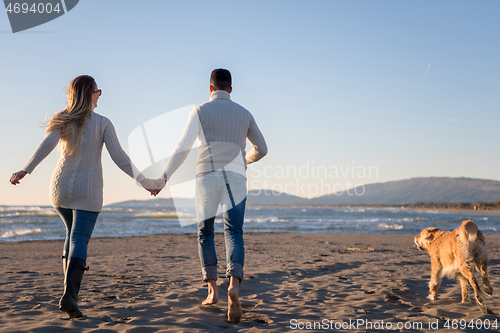 Image of couple with dog having fun on beach on autmun day