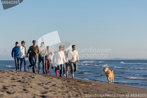 Image of Group of friends running on beach during autumn day