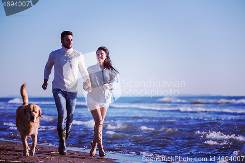 Image of couple with dog having fun on beach on autmun day