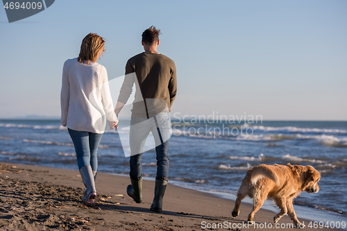 Image of couple with dog having fun on beach on autmun day