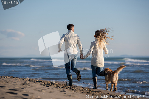 Image of couple with dog having fun on beach on autmun day