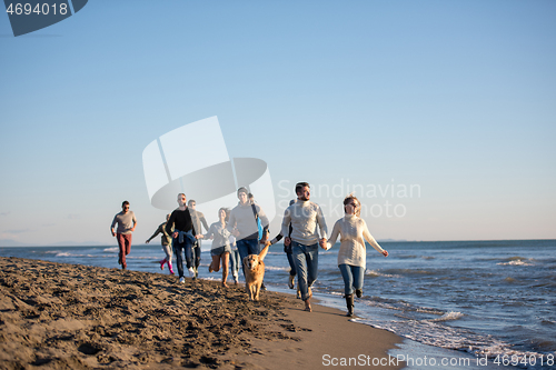 Image of Group of friends running on beach during autumn day
