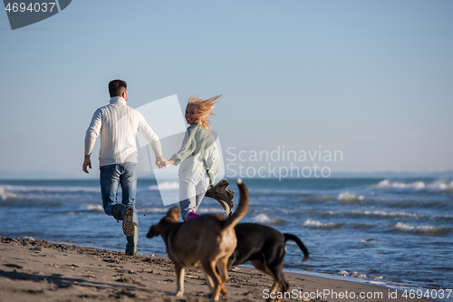 Image of couple with dog having fun on beach on autmun day