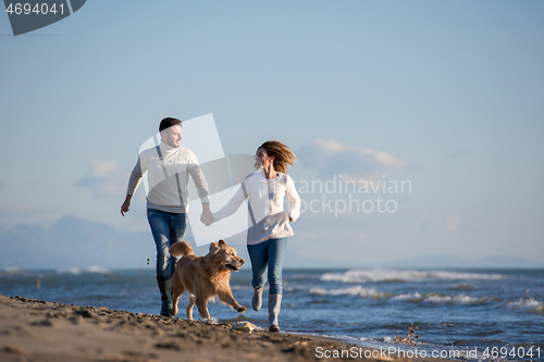 Image of couple with dog having fun on beach on autmun day