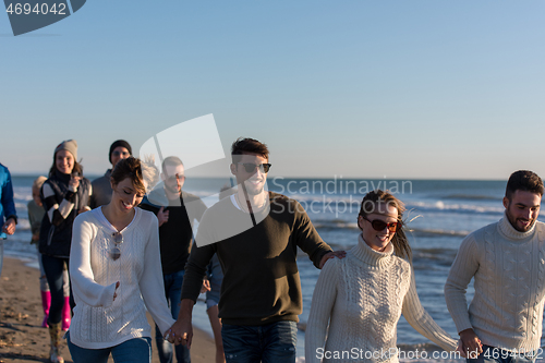 Image of Group of friends running on beach during autumn day