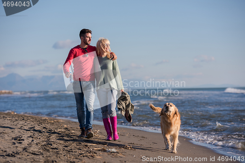 Image of couple with dog having fun on beach on autmun day