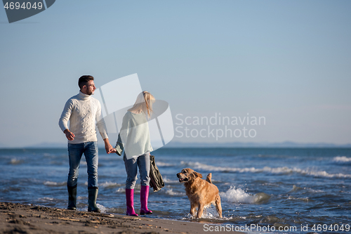 Image of couple with dog having fun on beach on autmun day