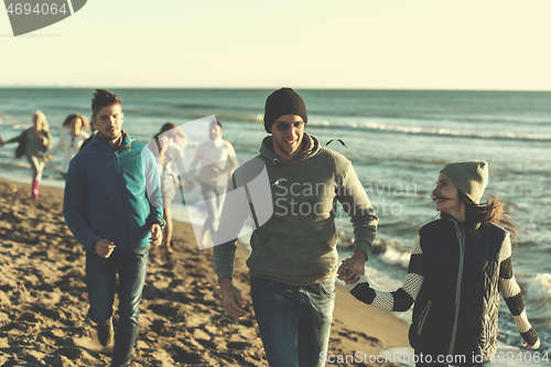 Image of Group of friends running on beach during autumn day