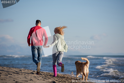 Image of couple with dog having fun on beach on autmun day