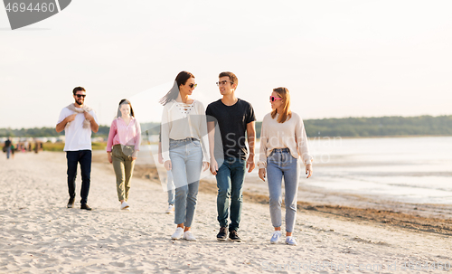 Image of happy friends walking along summer beach