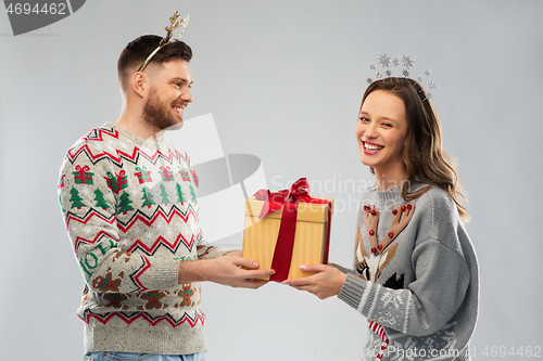 Image of happy couple in christmas sweaters with gift box