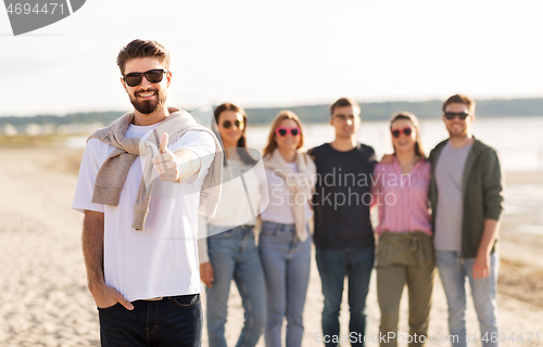 Image of happy man with friends on beach showing thumbs up