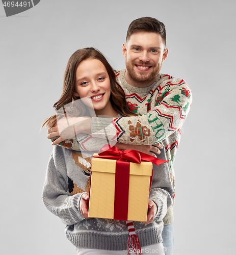 Image of happy couple in christmas sweaters with gift box