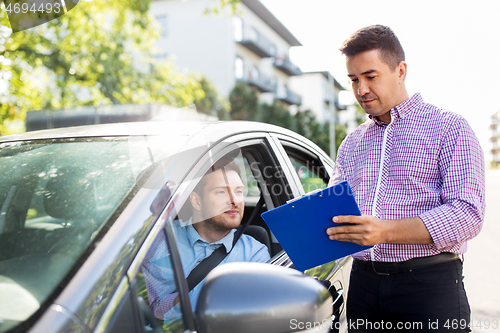 Image of car driving instructor with clipboard and driver