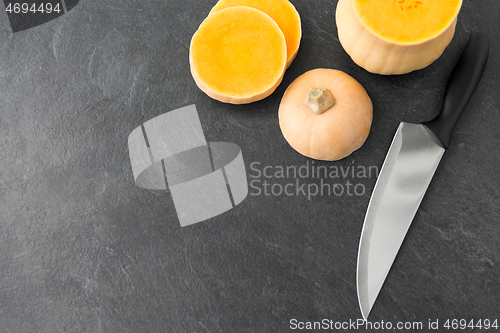 Image of cut pumpkin and kitchen knife on stone background