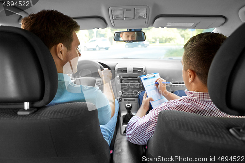 Image of car driving instructor with clipboard and driver