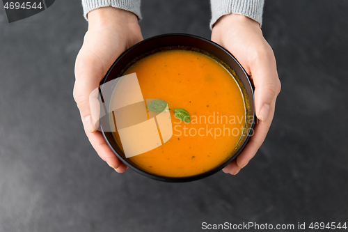 Image of hands with bowl of pumpkin cream soup on table