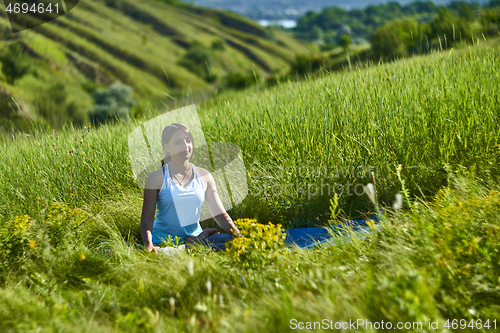 Image of Young female sitting in green grass meadow in summer day