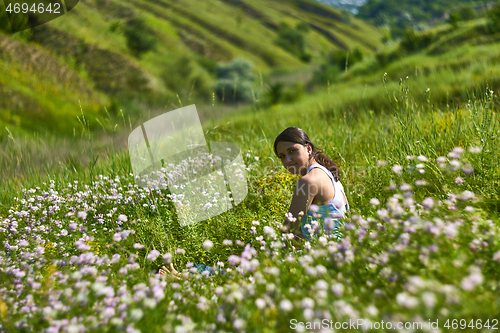 Image of Young female sitting in green grass meadow in summer day