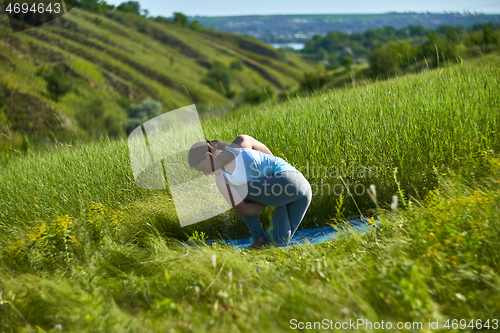 Image of Young woman doing yoga in green summer meadow