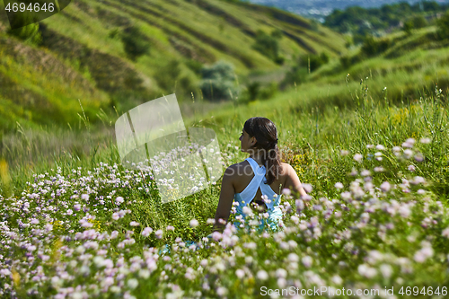 Image of Young female sitting in green grass meadow in summer day