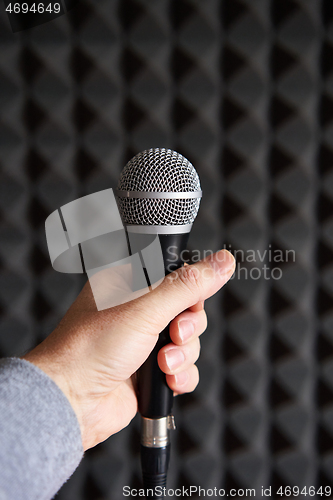 Image of Woman hand holding vocal mic on acoustic foam panel background