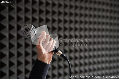 Image of Woman hand holding vocal mic on acoustic foam panel background