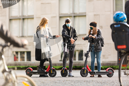 Image of Trendy fashinable group of friends riding public rental electric scooters in urban city environment at fall. New eco-friendly modern public city transport in Ljubljana, Slovenia