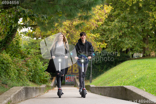 Image of Trendy fashinable teenagers riding public rental electric scooters in urban city park. New eco-friendly modern public city transport in Ljubljana, Slovenia