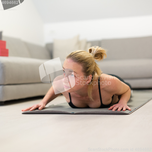 Image of Beautiful blonde woman doing home workout indoors. Woman practice yoga at home. Fit girl using workout tutorials for healthy active lifestyle. Woman using quarantine for home workouts.