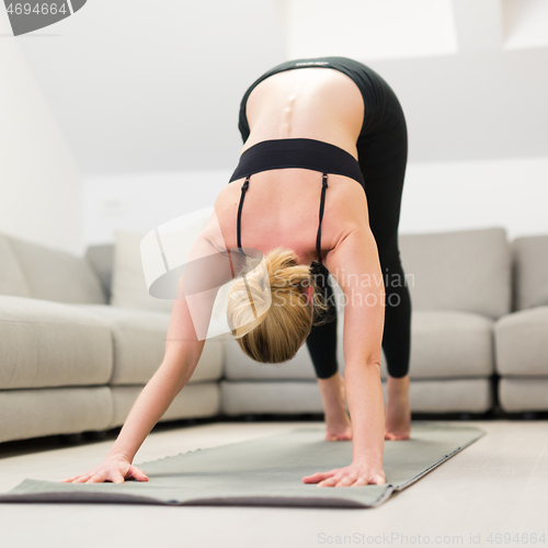 Image of Beautiful blonde woman doing home workout indoors. Woman practice yoga at home. Fit girl using workout tutorials for healthy active lifestyle. Woman using quarantine for home workouts.