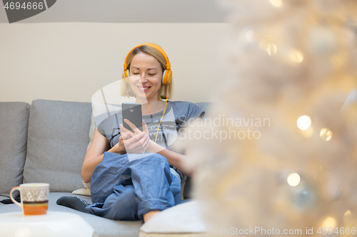 Image of Young cheerful woman sitting indoors at home living room sofa using social media on phone for video chatting and staying connected with her loved ones. Stay at home, social distancing lifestyle