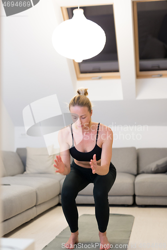 Image of Beautiful blonde woman doing home workout indoors. Woman practice yoga at home. Fit girl using workout tutorials for healthy active lifestyle. Woman using quarantine for home workouts.